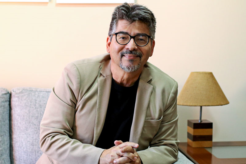 Pérsio Costa da Rosa, psicólogo, sentado em ambiente de consultório com luz natural